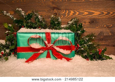 Christmas present gift wrapped in green paper with red ribbon with holly and snow against a wooden background, copy space for your own message.