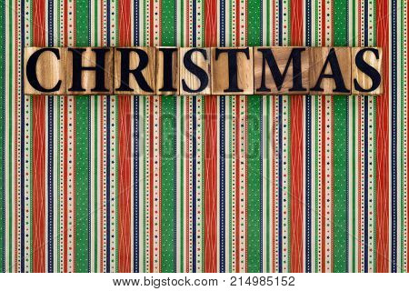 The word Christmas made from wooden block letters on a colourful striped background.