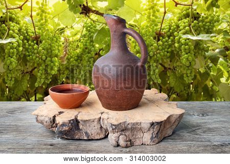 A Traditional Georgian Wine Jug And Clay Cups Filled With A Red Wine On The Wooden Table With Grapes