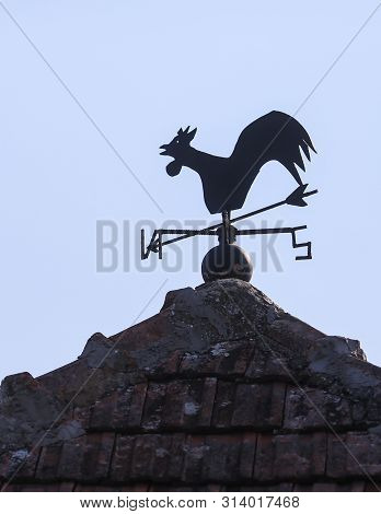 A Weather Vane (or Wind Vane, Weathercock) On Top Of A Building In A Rural Area