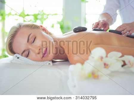 Beautiful young woman with eyes closed receiving hot stone massage at salon spa.