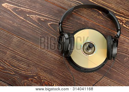 Headphones On Compact Disk And Copy Space. Black Headphones With Compact Discs On Brown Wooden Backg
