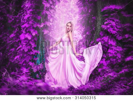 Beauty romantic young woman in long chiffon dress with gown posing in the fantasy forest in purple lush. Beautiful happy bride model girl enjoying nature outdoors, fluttering dress. Autumn garden