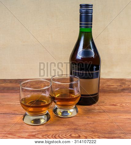 Two Portion Of Brandy In Brandy Bowls And Bottle Of Brandy On The Old Wooden Rustic Table