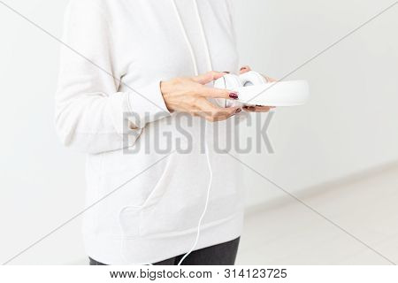 Close-up Of Indefinite Woman In Sweater Holding Headphones Standing On A White Background. Concept O