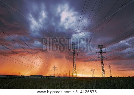 Extreme Weather. Electricity Pylons With Power Lines Against Stunning Storm At Sunset.