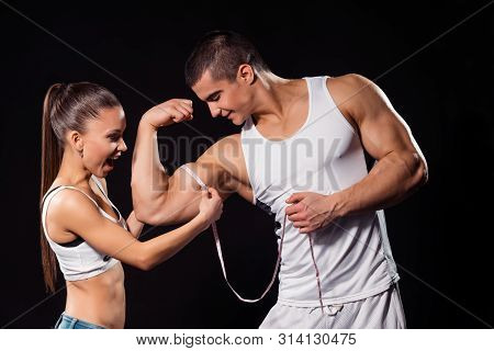 Excited Girl Measuring Bodybuilders Bicep. Young Athletes On Dark Background. Hes Become Much Bigger