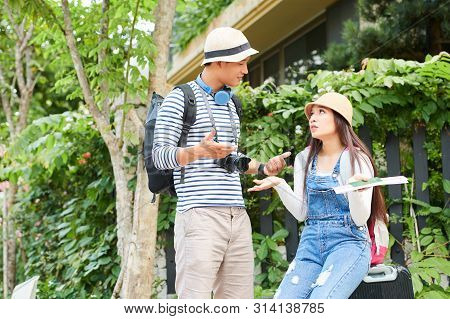 Tourirts With Backpacks And Suitcase Actively Gesturing When Discussing How To Get From The Hotel To