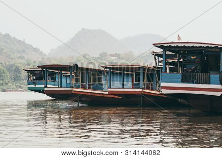 Traditional Laotian Wooden Slow Boats On Mekong River Near Luang Prabang At Sunset, Laos. Mountain O