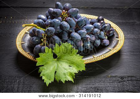 Bunch Of Ripe Blue-black Table Grapes With Leaf Served On Black Plate On Black Wooden Background