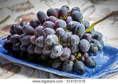 Bunch Of Ripe Blue-black Table Grapes With Leaf Served On Blue Plate As Sweet Fruit Dessert