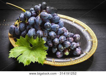Bunch Of Ripe Blue-black Table Grapes With Leaf Served On Blue Plate As Sweet Fruit Dessert