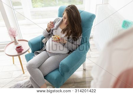 Beautiful Pregnant Woman Sitting In An Armchair, Eating Mixed Seasonal Vegetables Salad; Pregnancy A