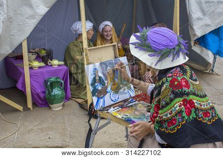 Moscow/ Russia - 15.06.2019: Woman Painter In A Lavender Hat Draws On Canvas People Sitting In An Ol