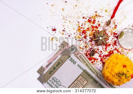 Close View Of Elegant Rakhi With Scattered Rice, Kumkum, Turmeric And Sugar Rock, Cardamom, And Swee