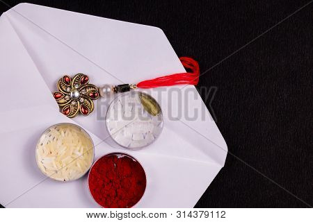 Indian Festival Concept - Elegant Rakhi In A White Envelope With Rice Grains, Kumkum, Sugar Rock And