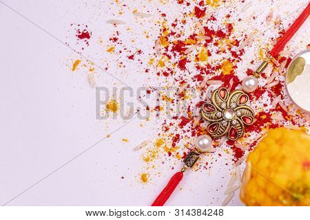 Raksha Bandhan Background With A Rakhi, Scattered Kumkum, Rice Grains, Haldi And Cardamom, Sweets On