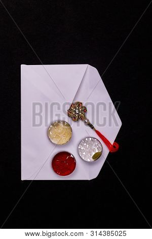 Raksha Bandhan Concept - Rakhi In A White Envelope With Rice Grains, Kumkum, Sugar Rock And Cardamom