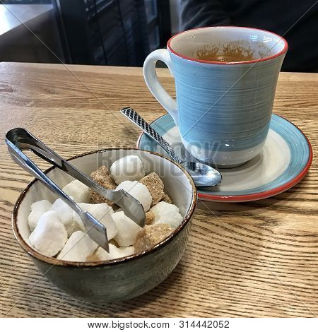 Coffee And Sugar On A Cafe Table Close To A Window. Nice Blue Coffee Cup, Saucer And A Teaspoon. Fan