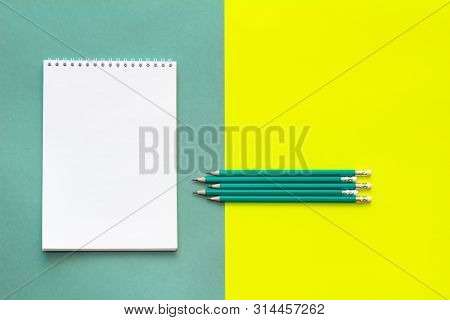 White Wideopen Blank Clean Notepad Page And Green Pencils On Yellow-green Table.