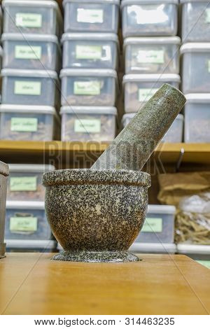 Vintage Mortar In Herbal Store With Blur Herb Shelf Behind, Thailand.