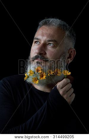 Portrait Of A Pensive Brutal Man With A Gray Beard Decorated With Yellow Flowers On A Black Backgrou