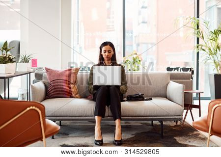 Businesswoman Sitting On Sofa Working On Laptop At Desk In Shared Workspace Office