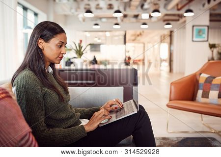 Businesswoman Sitting On Sofa Working On Laptop At Desk In Shared Workspace Office