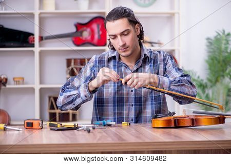 Young handsome repairman repairing violin