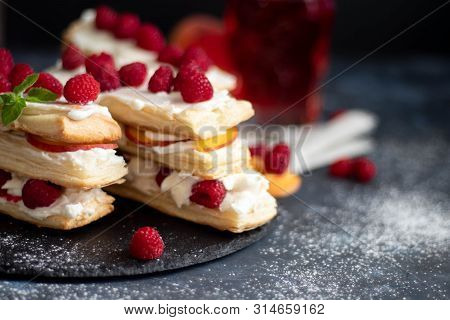 Dessert Milfey. Strips Of Puff Pastry With Curd Cream Raspberry Berries And Peach Slices. In The Bac