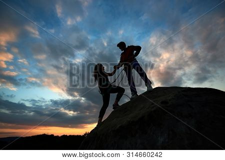 Two Climbers Reaching Summit One Holding Hand Of His Partner Assisting To Make Last Step To Top. Tea