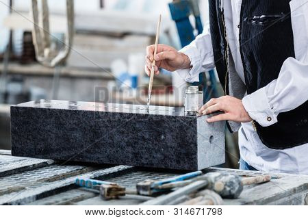 Stonemason painting in engraving with silver paint and brush
