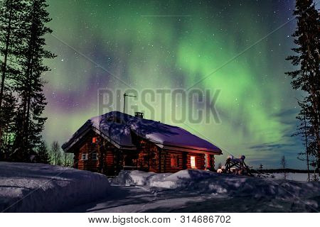 Polar Arctic Northern Lights Aurora Borealis Activity Over The Wooden House In Winter Finland, Lapla