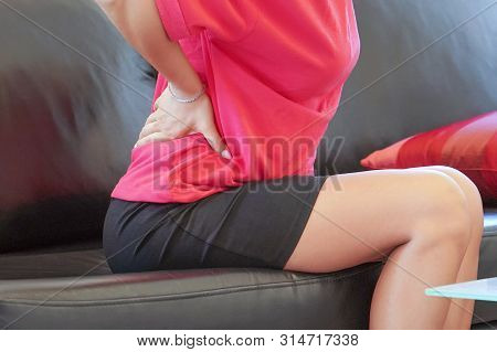 Close-up View Of A Young Woman With Pain In Kidneys At Home On Couch. Young Woman With Back Ache Cla