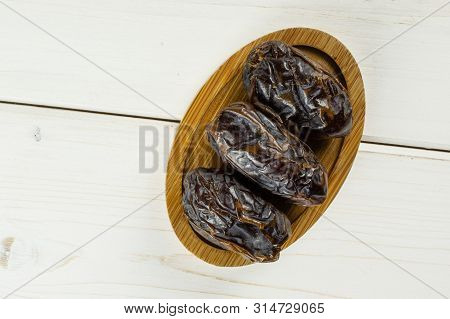 Group Of Three Whole Dried Brown Date Medjool On Bamboo Plate Flatlay On White Wood