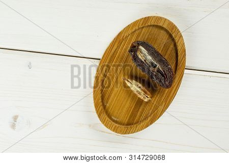 Group Of One Half One Piece Of Dried Brown Date Medjool On Bamboo Plate Flatlay On White Wood