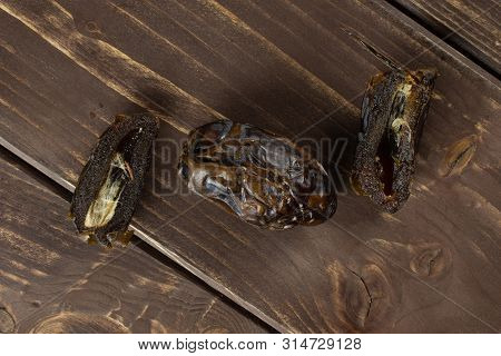 Group Of One Whole Two Halves Of Dried Brown Date Medjool Flatlay On Brown Wood