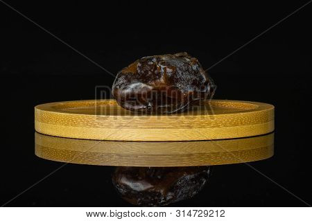 One Whole Dried Brown Date Medjool On Bamboo Plate Isolated On Black Glass