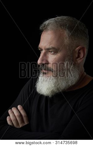 Portrait Of A Brutal Gray Haired Man With A Gray Lush Beard And Strict Face On A Black Background, S
