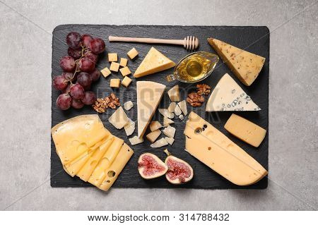 Slate Board With Different Types Of Delicious Cheese And Snacks On Grey Table, Top View