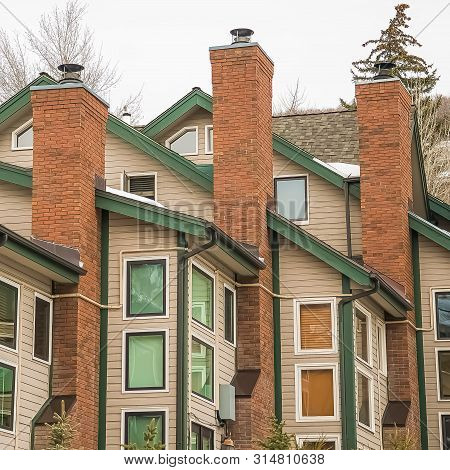 Square Homes With White Wall Sidings And Red Brick Chimneys Against Cloudy Sky
