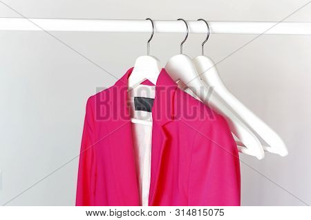 Bright Pink Women's Jacket On White Wooden Coat Hanger On Rod Against Light Gray Wall Flat Lay Copy 