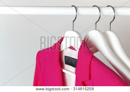Bright Pink Women's Jacket On White Wooden Coat Hanger On Rod Against Light Gray Wall Flat Lay Copy 