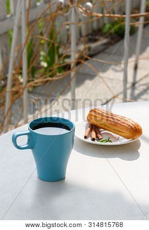 Aromatic Coffee In A Blue Cup With Eclairs In A Summer Cafe.