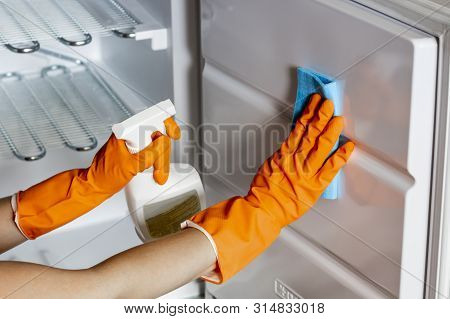 Female Hands In Protective Gloves Are Wiping Refrigerator Inside Using A Spray And A Duster Close Up