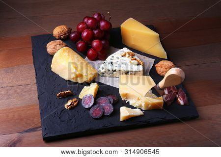 Assortment Of Cheese With Fruits, Grapes, Nuts And Cheese Knife On A Wooden Serving Tray.