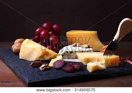 Assortment Of Cheese With Fruits, Grapes, Nuts And Cheese Knife On A Wooden Serving Tray.