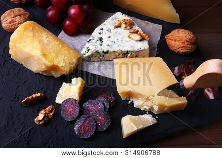 Assortment Of Cheese With Fruits, Grapes, Nuts And Cheese Knife On A Wooden Serving Tray.