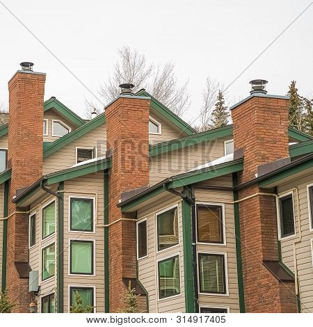 Square Frame Homes With White Wall Sidings And Red Brick Chimneys Against Cloudy Sky