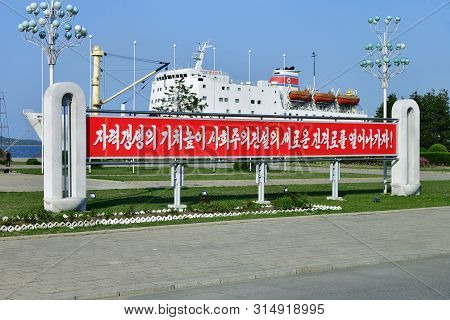 Wonsan, North Korea - May 3, 2019: Propaganda Banner And The Man Gyong Bong 92 Cargo-passenger Ferry